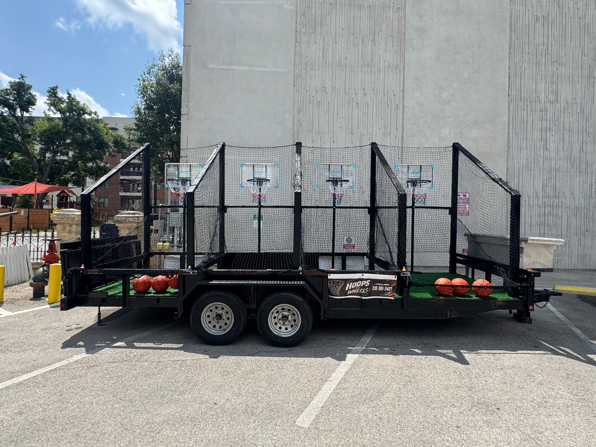 The Hoops on Wheels trailer parked outdoors with all four netted basketball stations open and basketballs lined up on the turf deck