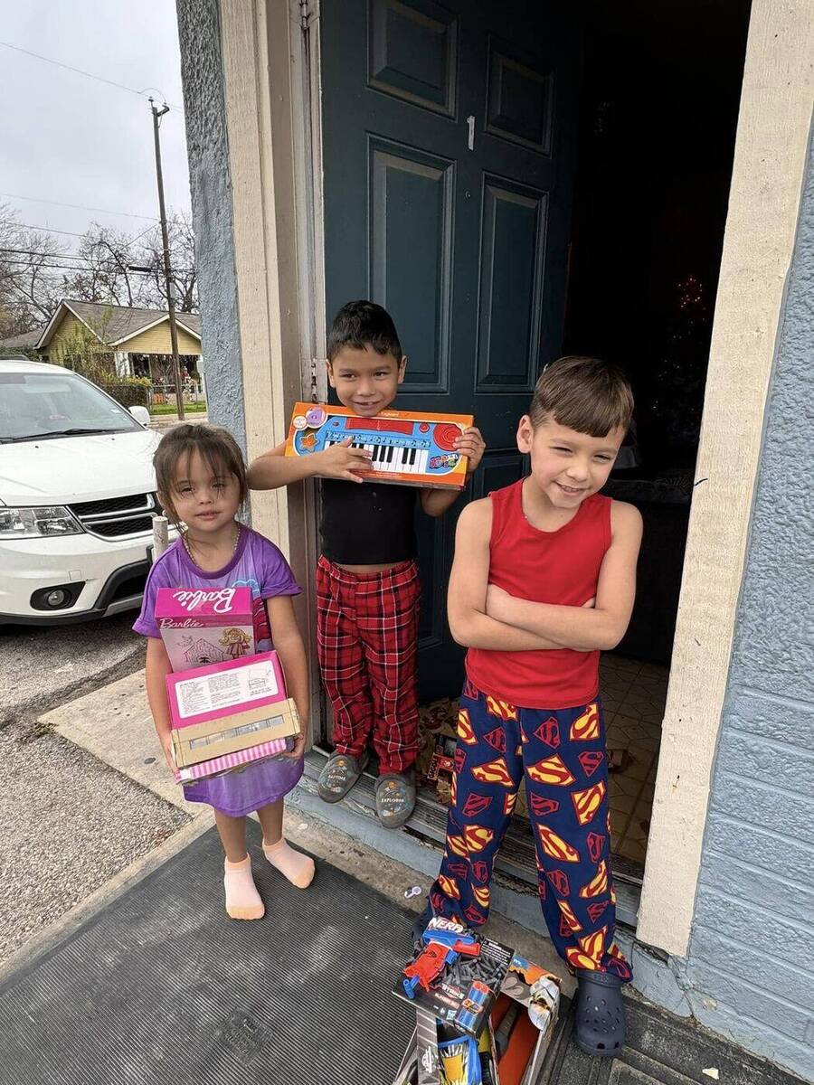 Three children at their front door holding Christmas toys delivered by the Doodle Train family during a local community giveback visit